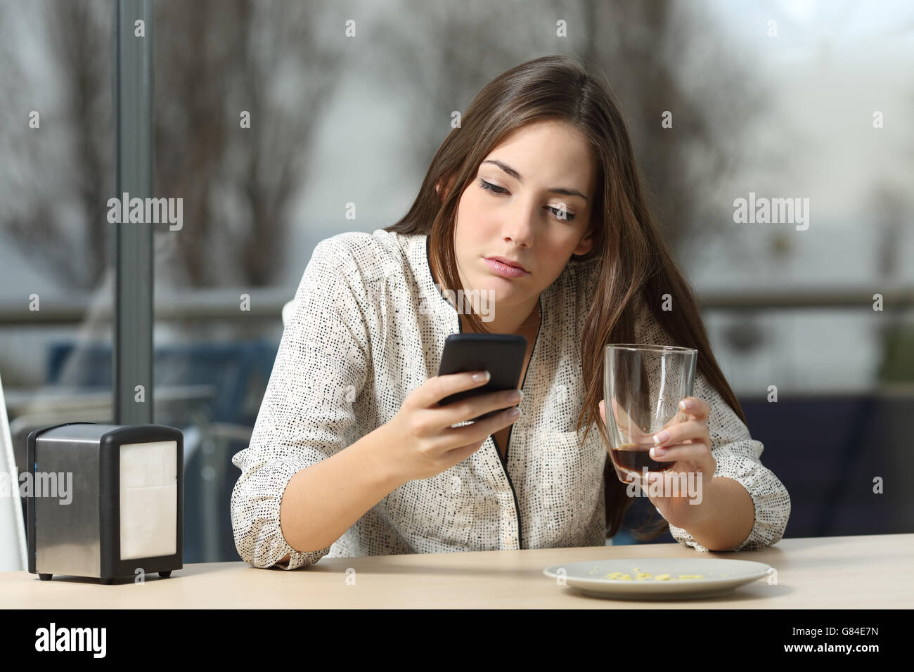 Angry woman stood up in a date in a coffee shop searching for messages and lost calls in a smart phone Stock Photo