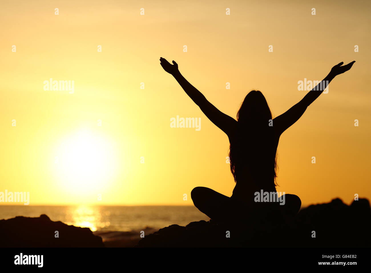Back view portrait silhouette of a happy woman raising arms in a new day looking at warm sun at sunrise Stock Photo