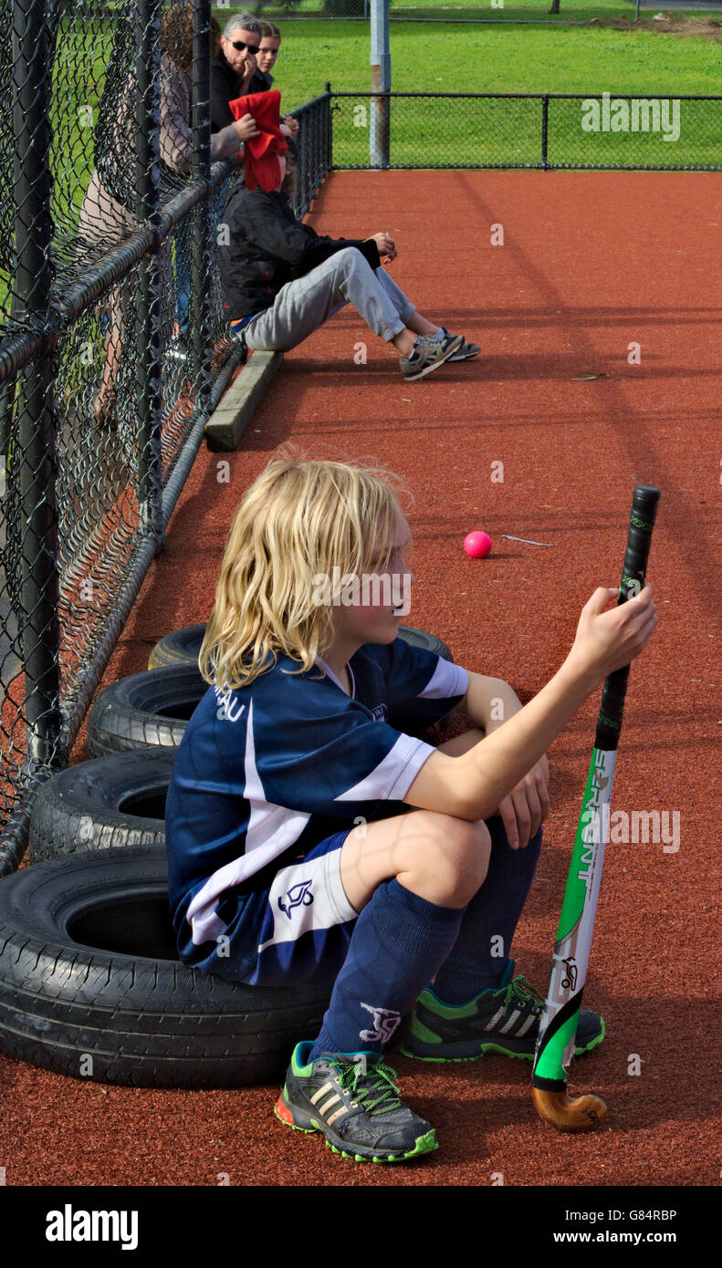 Young hockey player sitting on a tyre on the sidelines, staring out at the game. Stock Photo