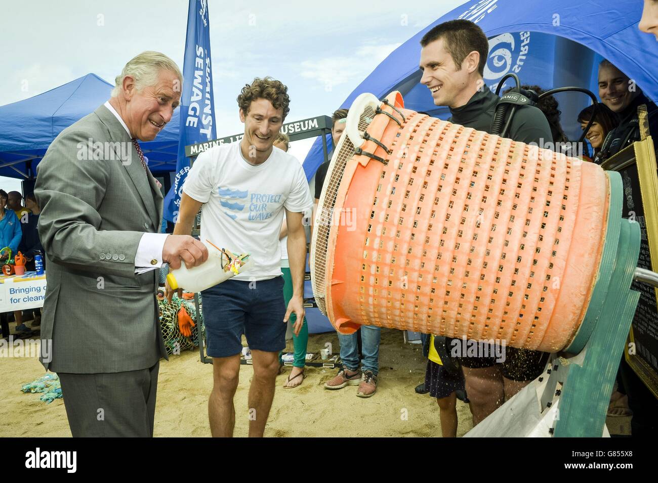 The Prince of Wales uses a recycled plastic milk carton to scoop beach litter to demonstrate a hand operated sand sifter, which filters out marine debris collected from beaches, during his visit to Fistral Beach, Newquay, as part of a Royal tour of Cornwall. Stock Photo