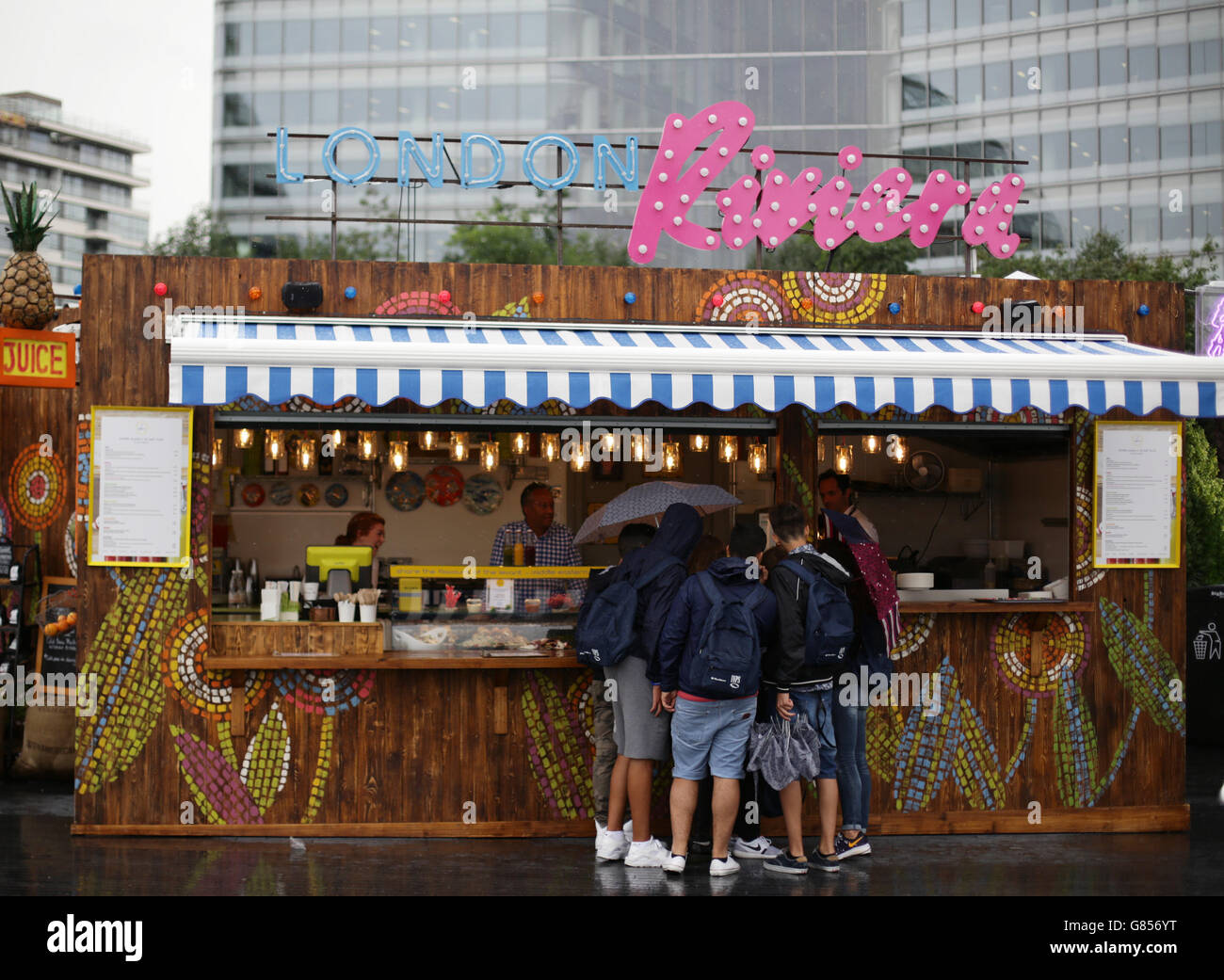 People walking past the London Riviera food and drink stall on More London Riverside during a rain shower as parts of Britain are set to be battered by very heavy rain and winds of up to 50mph in an 'intense' day of unseasonably bad weather. Stock Photo