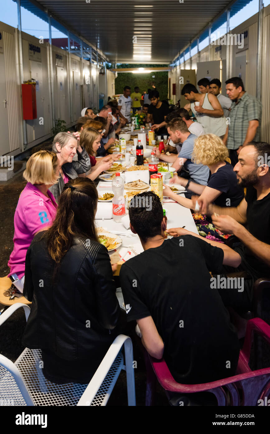Scharnhausen, Germany - June 22.06.2016: Male Muslim refugees and German volunteers (men and women) sit together eating dinner d Stock Photo