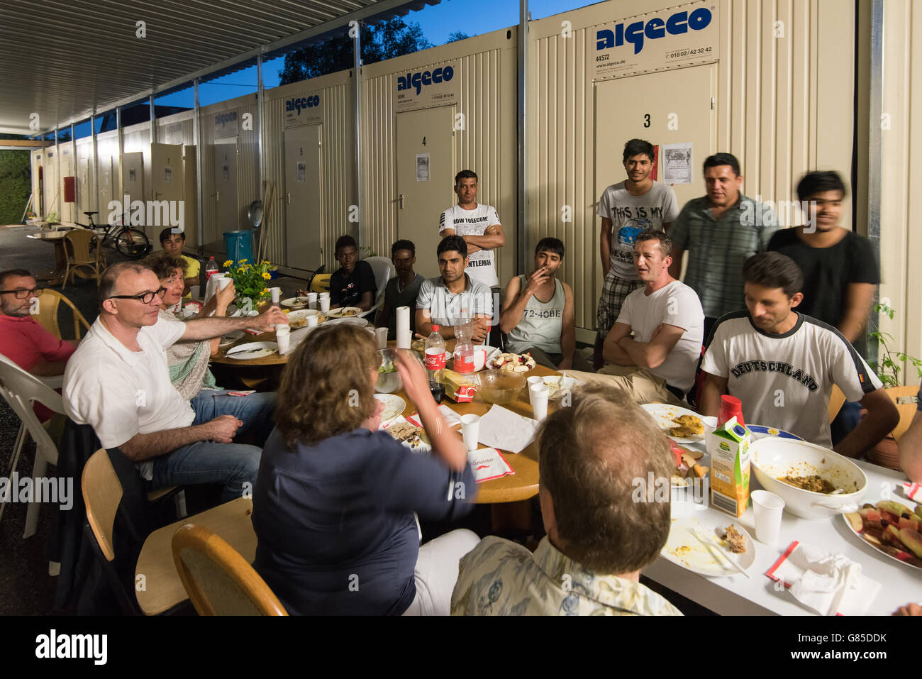 Scharnhausen, Germany - June 22.06.2016: Male Muslim refugees and German volunteers (men and women) sit together eating dinner d Stock Photo