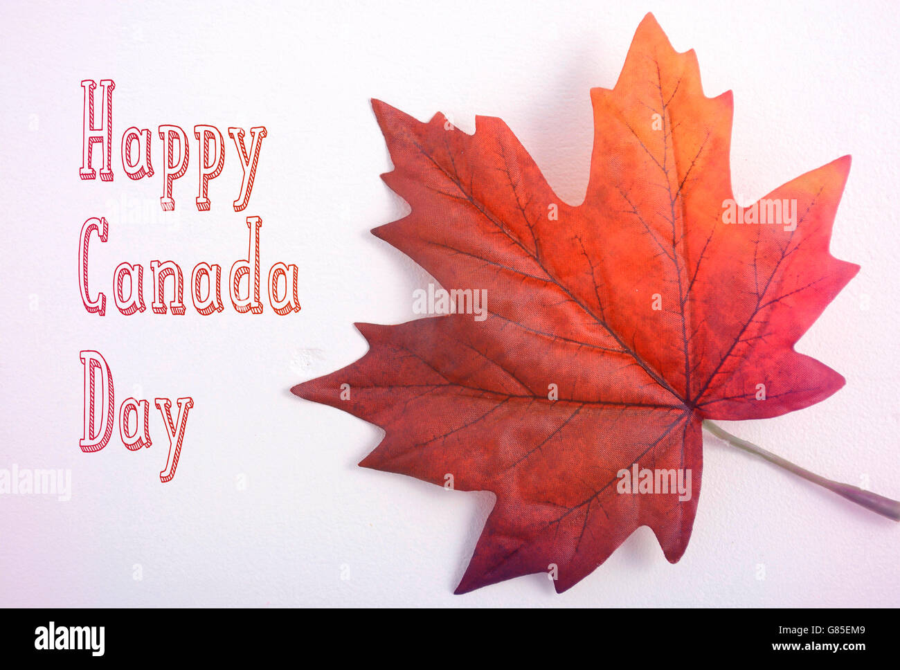 Happy Canada Day symbolic maple leaf on a white wood table with added light leak filters and on-trend handdrawn text. Stock Photo