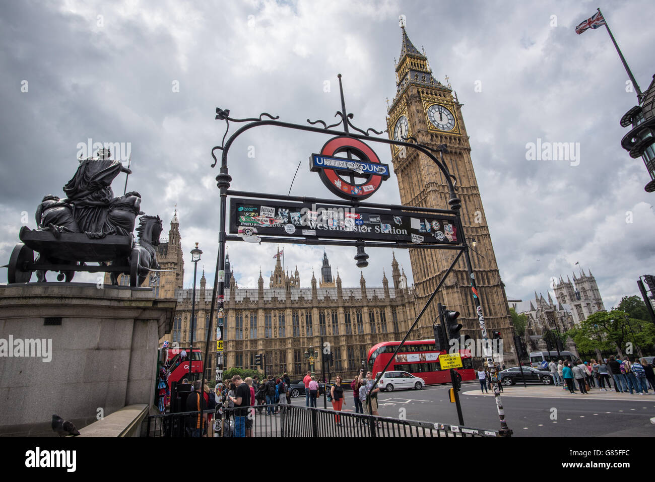 The Houses of Parliament in London seen through the Westminster Underground sign on a cloudy day with the statue of Boudica Stock Photo