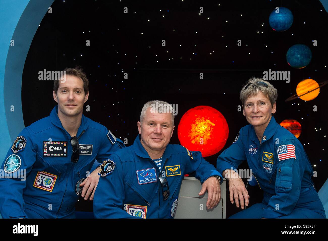 International Space Station crew Expedition 49 backup crew members pose in front of a mural of the planets during a tour of a museum June 26, 2016 in Baikonur, Kazakhstan. Members from L-R:   ESA astronaut Thomas Pesquet, Russian cosmonaut Oleg Novitskiy and American astronaut Peggy Whitson. Stock Photo