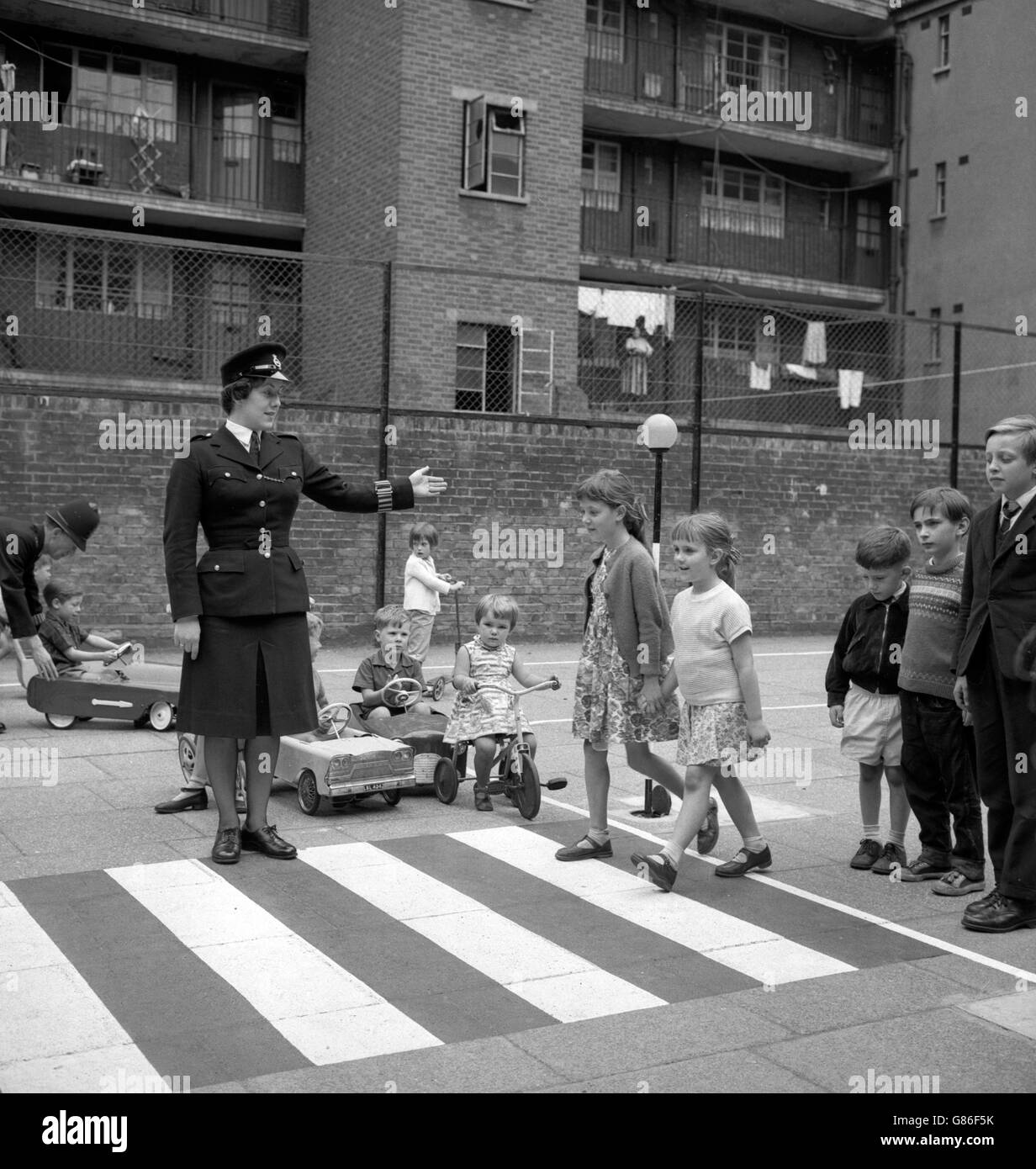 WPC M. Cleland holds up the 'traffic' as Catherine Patricia Gilmen, 6, and Karen Valerie Greene, 9, walk over a pedestrian crossing during demonstrations at the Road Safety Training Area in Bloomsbury, London. Stock Photo