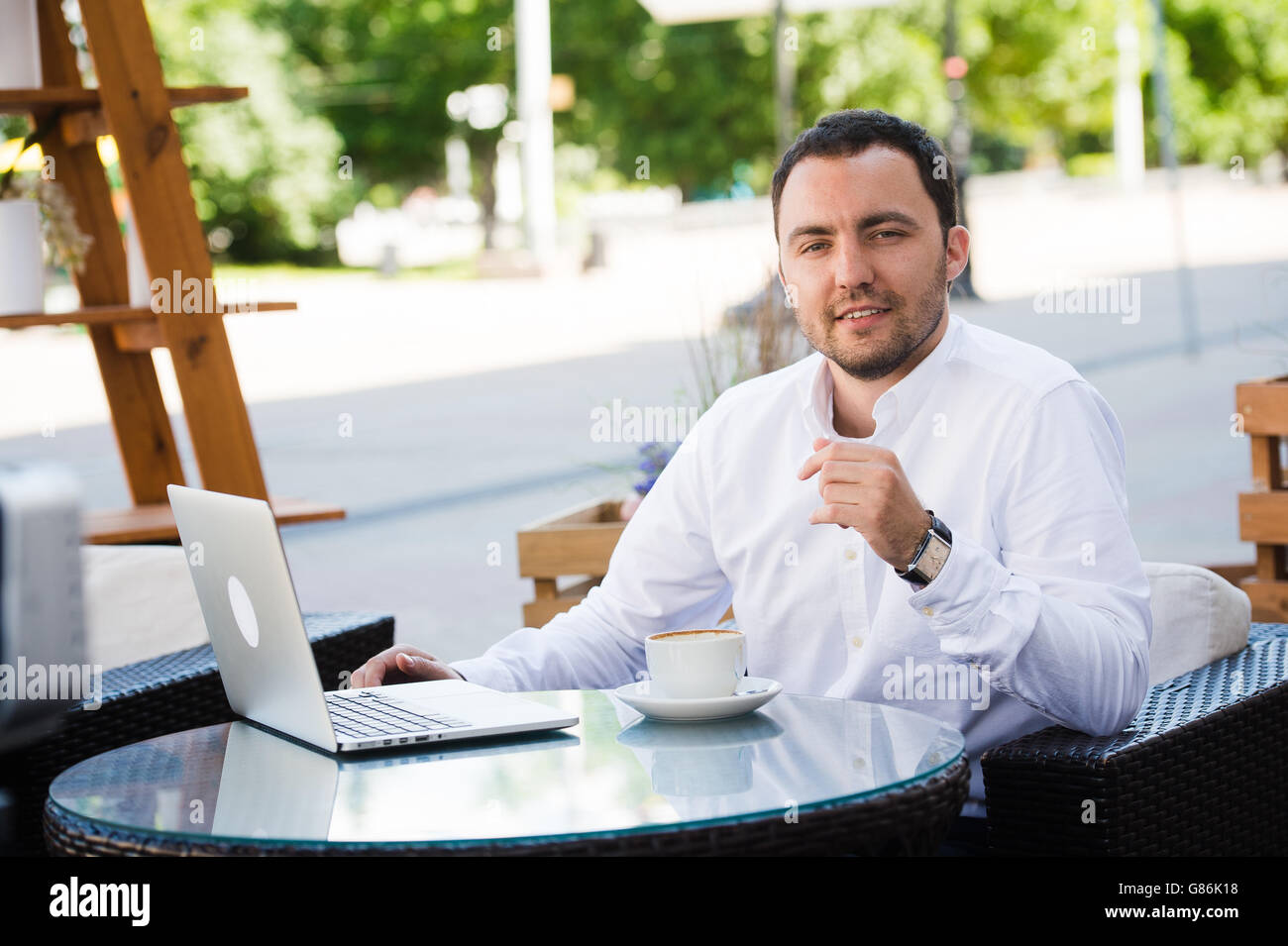 Young handsome man smiling and drinking coffee in a seaside restaurant. He is happy, looking at camera Stock Photo