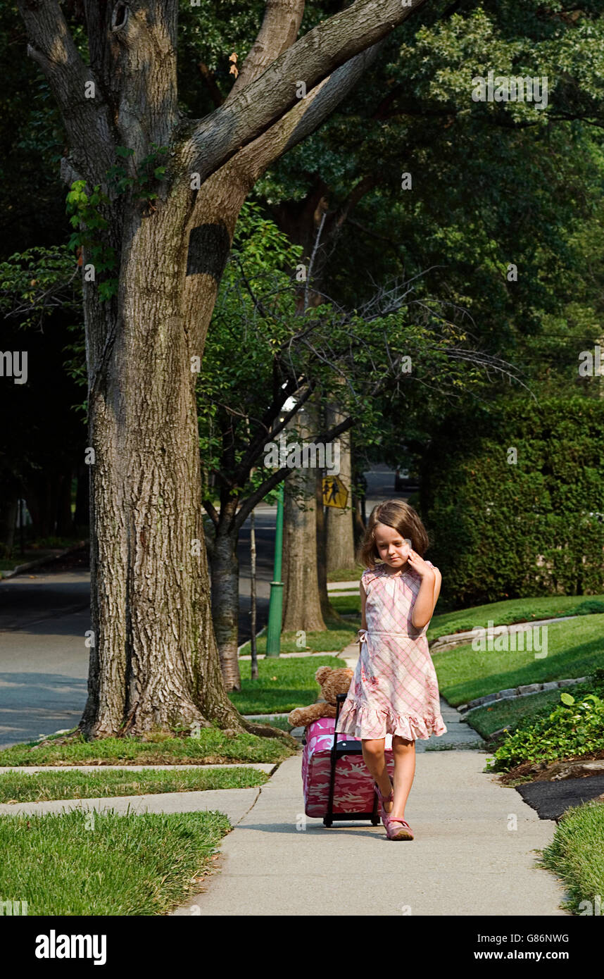 A young girl pulling a suitcase on the sidewalk. Stock Photo