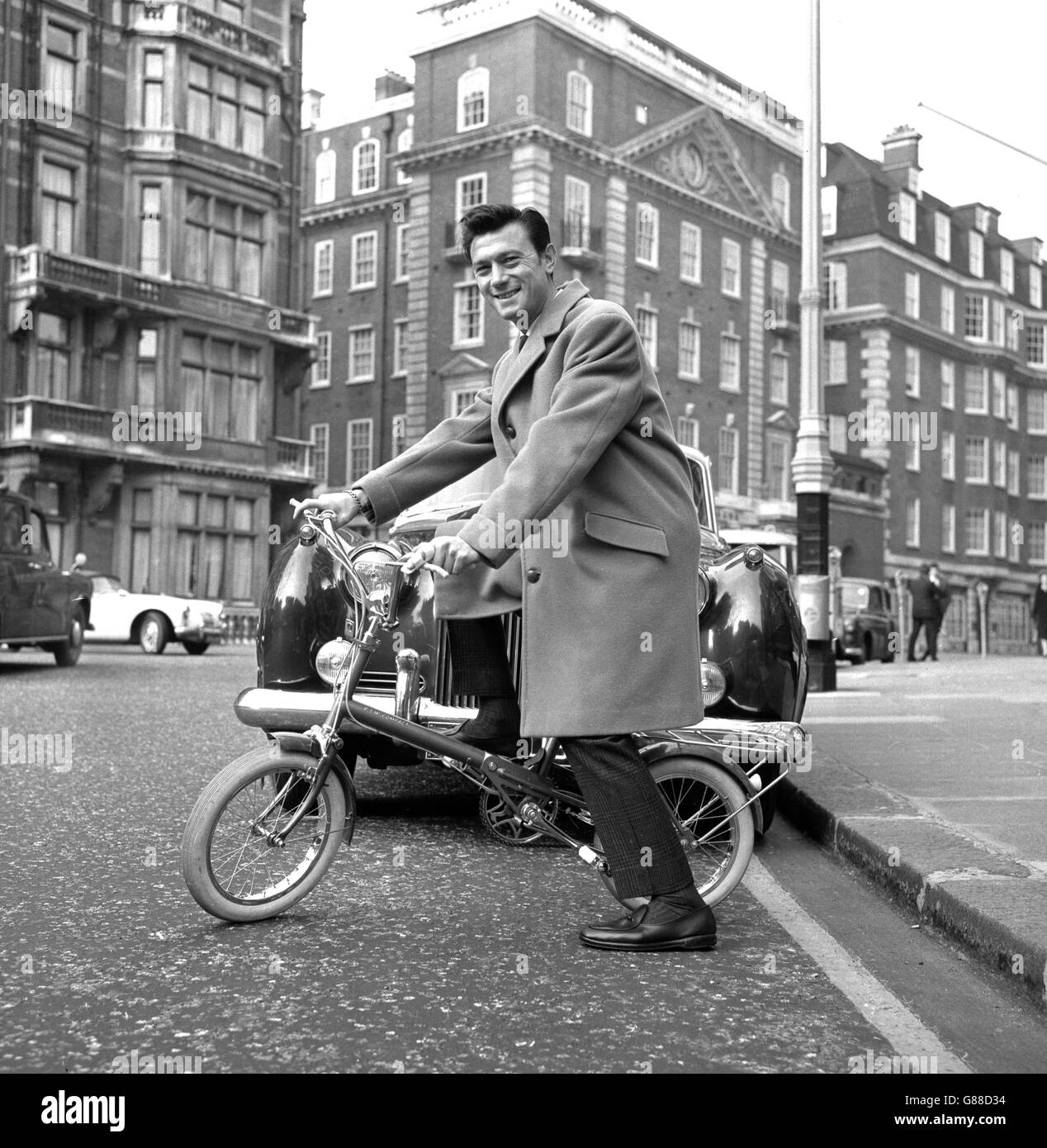 Film star Laurence Harvey has found two wheels the best means of beating the traffic jams in big cities. He bought this Raleigh Compact folding bicycle, which packs easily into the boot of his car. If necessary, he can park on the outskirts and cycle in. Laurence, star of 'Life at the Top', purchased the bike in London so that he could take it back to the States. Stock Photo