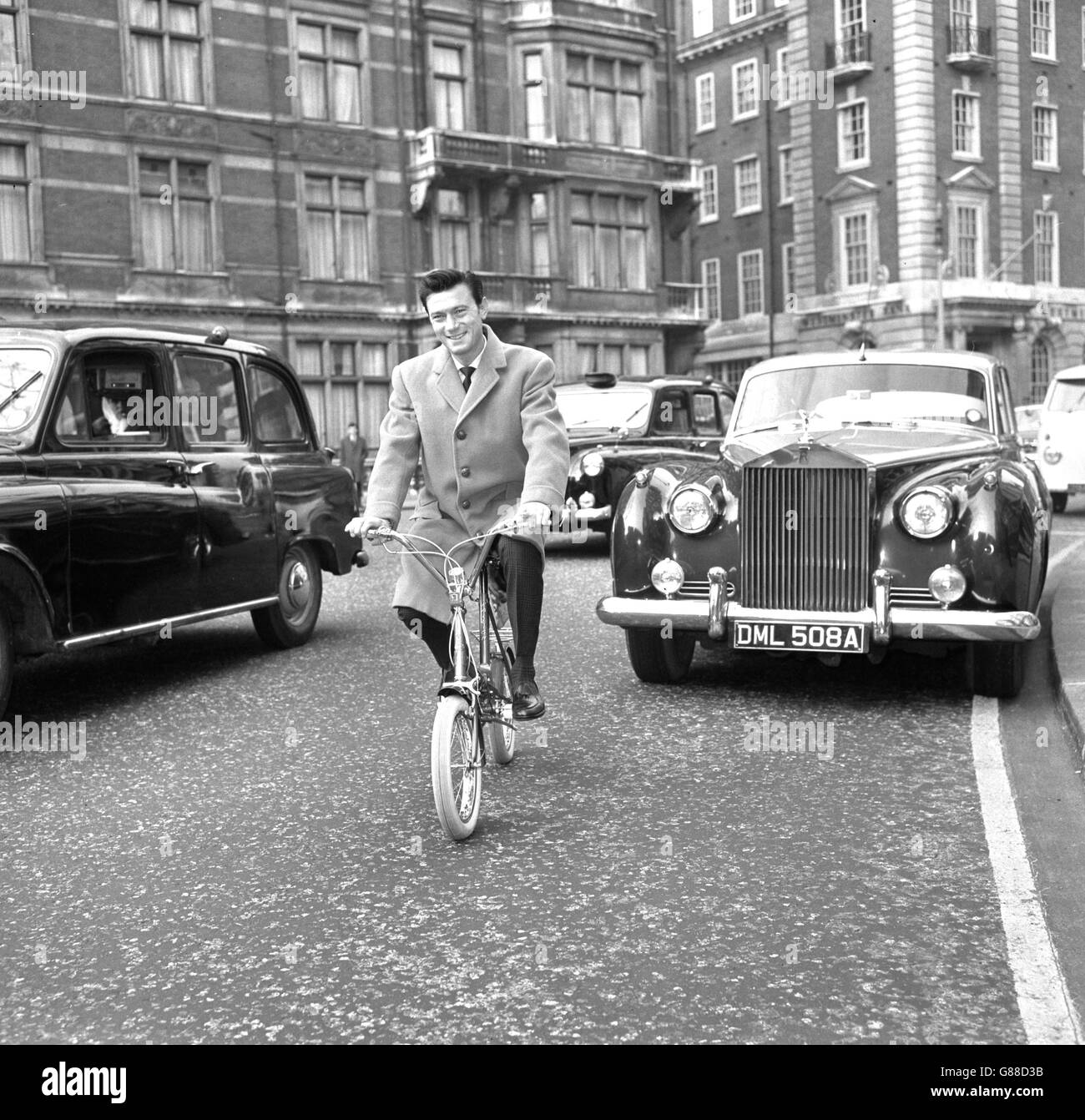 Film star Laurence Harvey has found two wheels the best means of beating the traffic jams in big cities. He bought this Raleigh Compact folding bicycle, which packs easily into the boot of his car. If necessary, he can park on the outskirts and cycle in. Laurence, star of 'Life at the Top', purchased the bike in London so that he could take it back to the States. Stock Photo