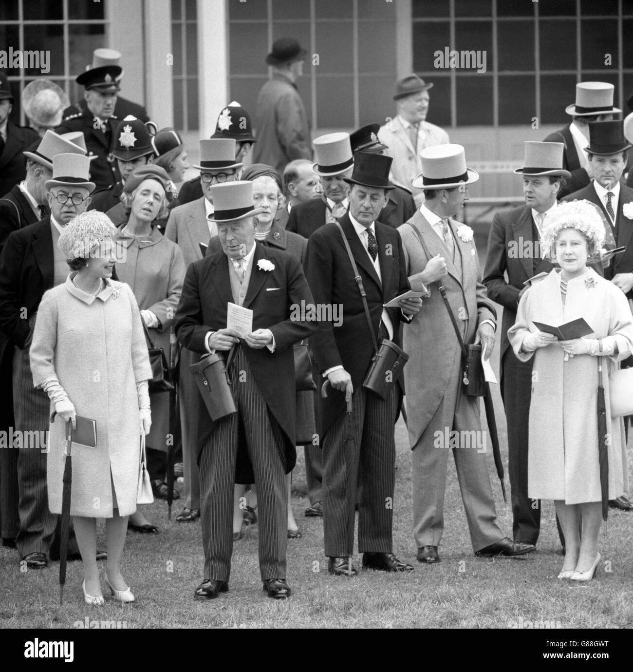 Both Queen Elizabeth II (l), seen chatting to the Duke of Norfolk, and the Queen Mother (extreme right) had umbrellas when they watched the parade of runners for the Oaks Stakes at Epsom Races. Stock Photo