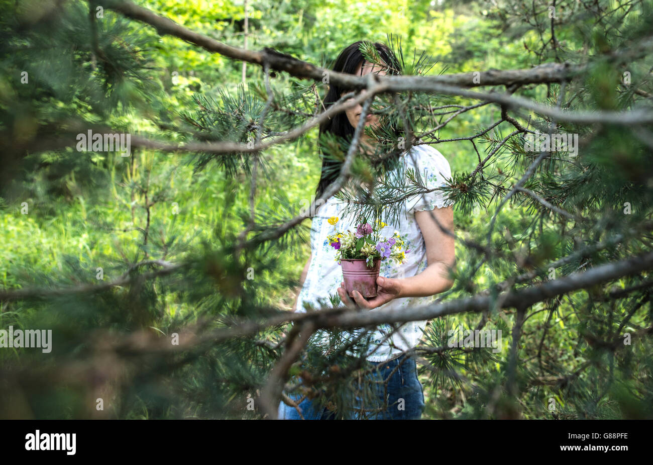 Woman holding a flower pot with wildflowers in forest Stock Photo