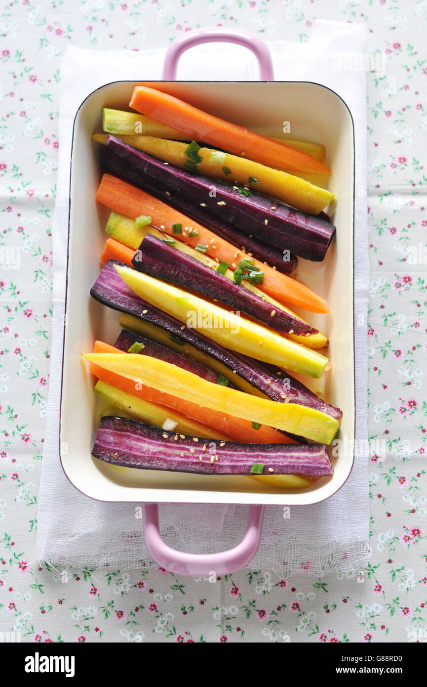 Overhead view of orange, purple and yellow carrots in baking dish Stock Photo