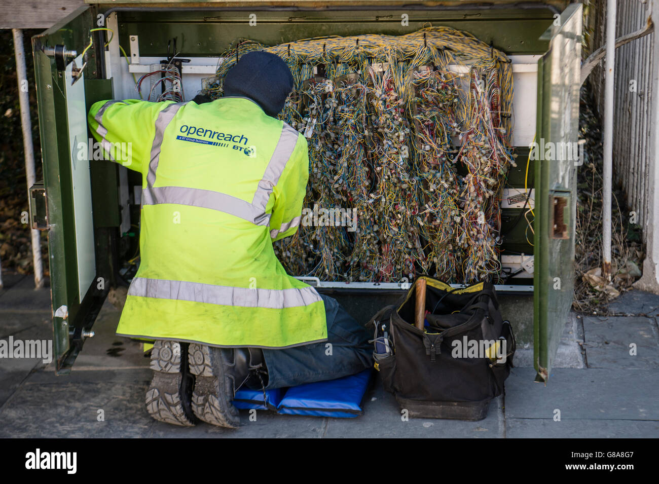 A rear view of a BT (British Telecom) engineer at work at a street corner green junction box for fibre broadband, UK Stock Photo