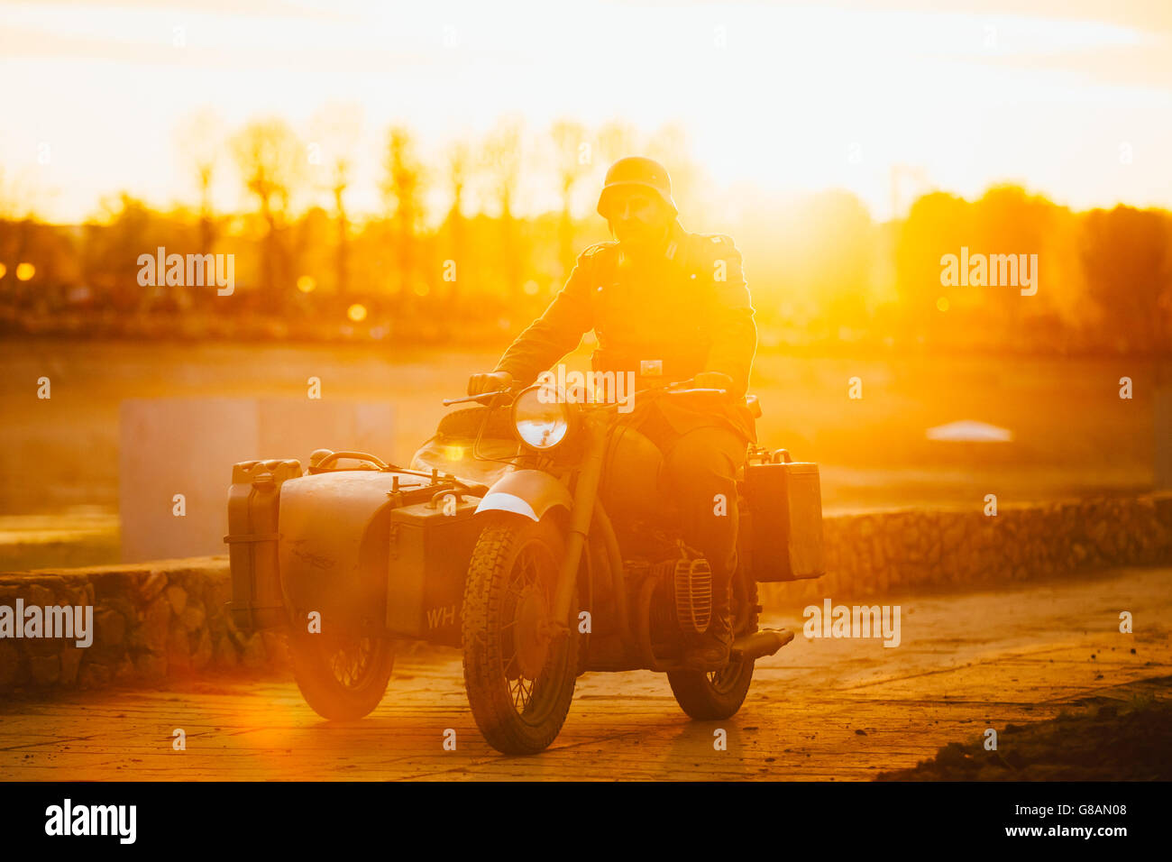 Unidentified re-enactor dressed as World War II german wehrmacht soldier rides on motorcycle in  rays of sunset sun. Stock Photo