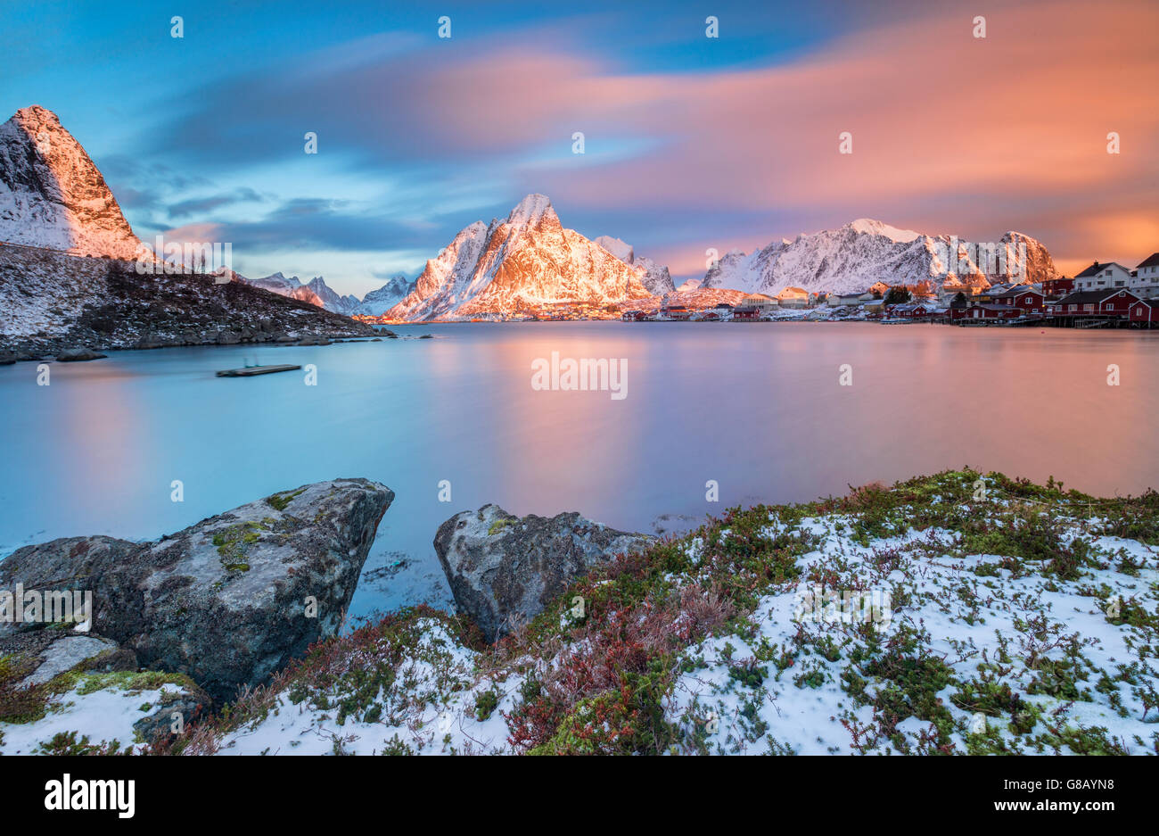 The pink sky at sunrise illuminates Reine village with its cold sea and the snowy peaks Lofoten Islands Northern Norway Europe Stock Photo