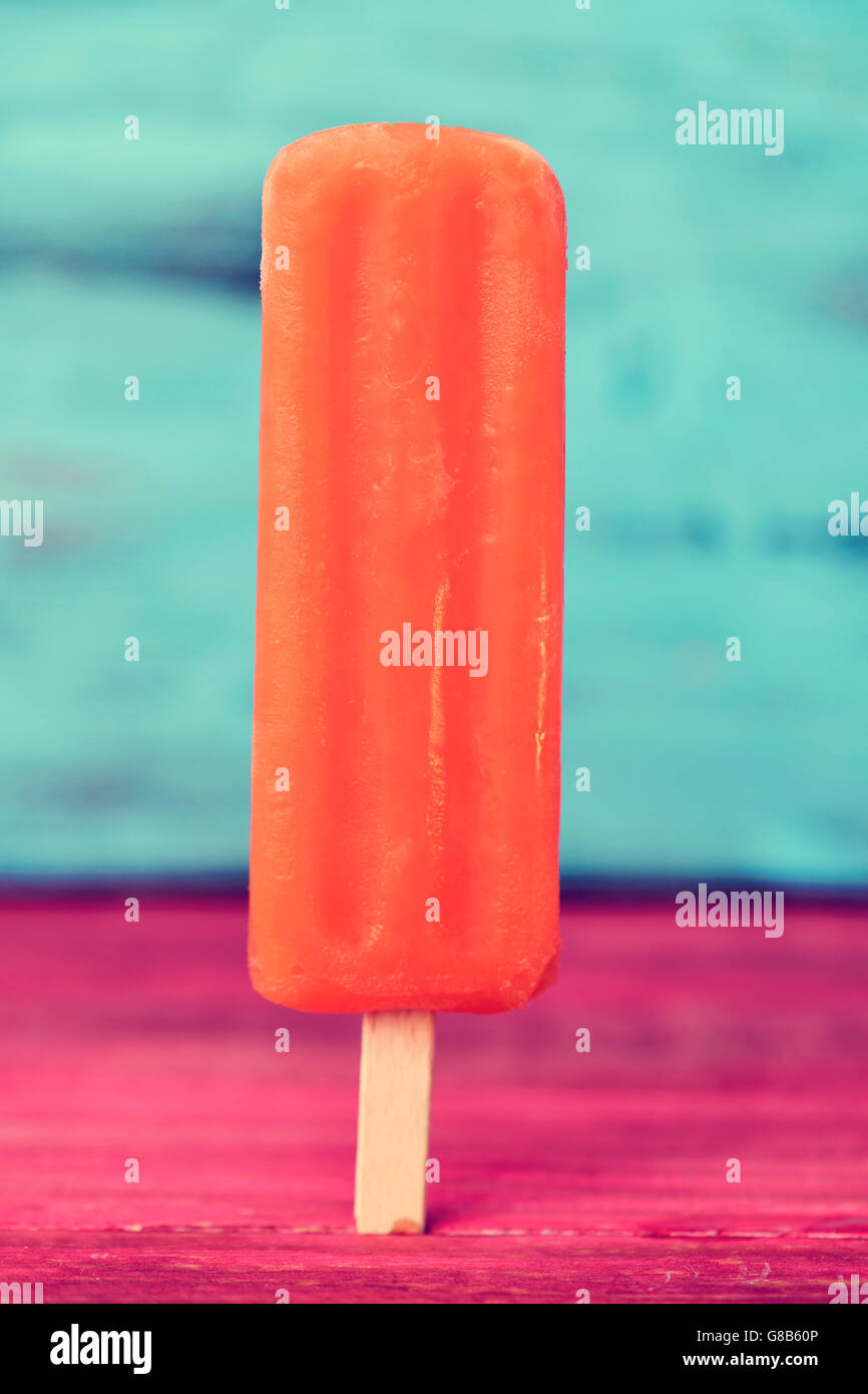 a refreshing orange flavored ice pop on a red rustic wooden table, against a rustic blue wooden background Stock Photo