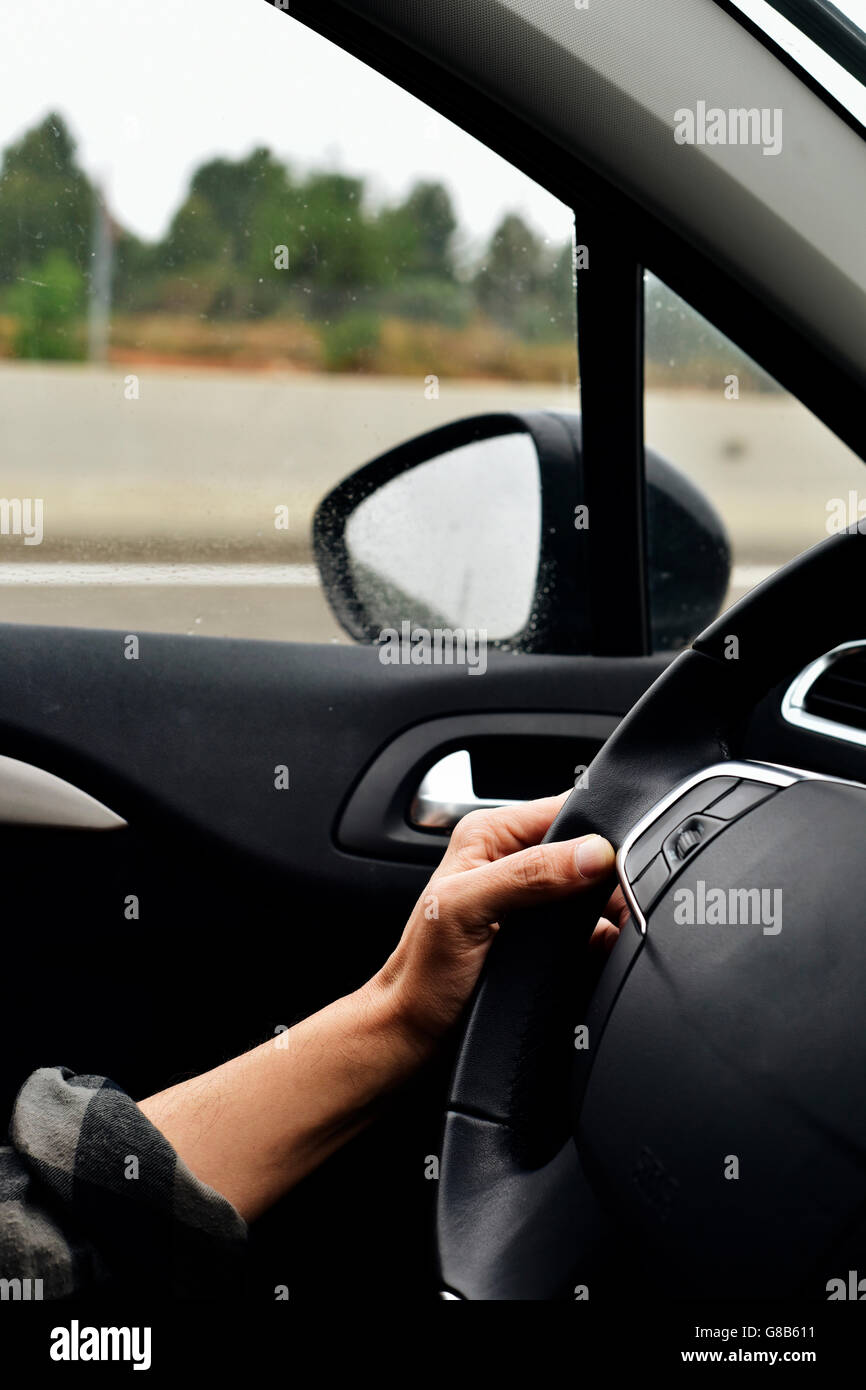 closeup of a young caucasian man driving a car in a road with several lanes, in a rainy day Stock Photo