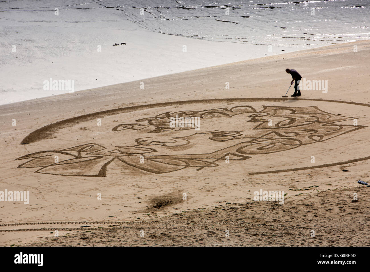 UK, Wales, Ceredigion, New Quay, Beach, sand artist Marc Traynor raking picture of Dylan Thomas Stock Photo