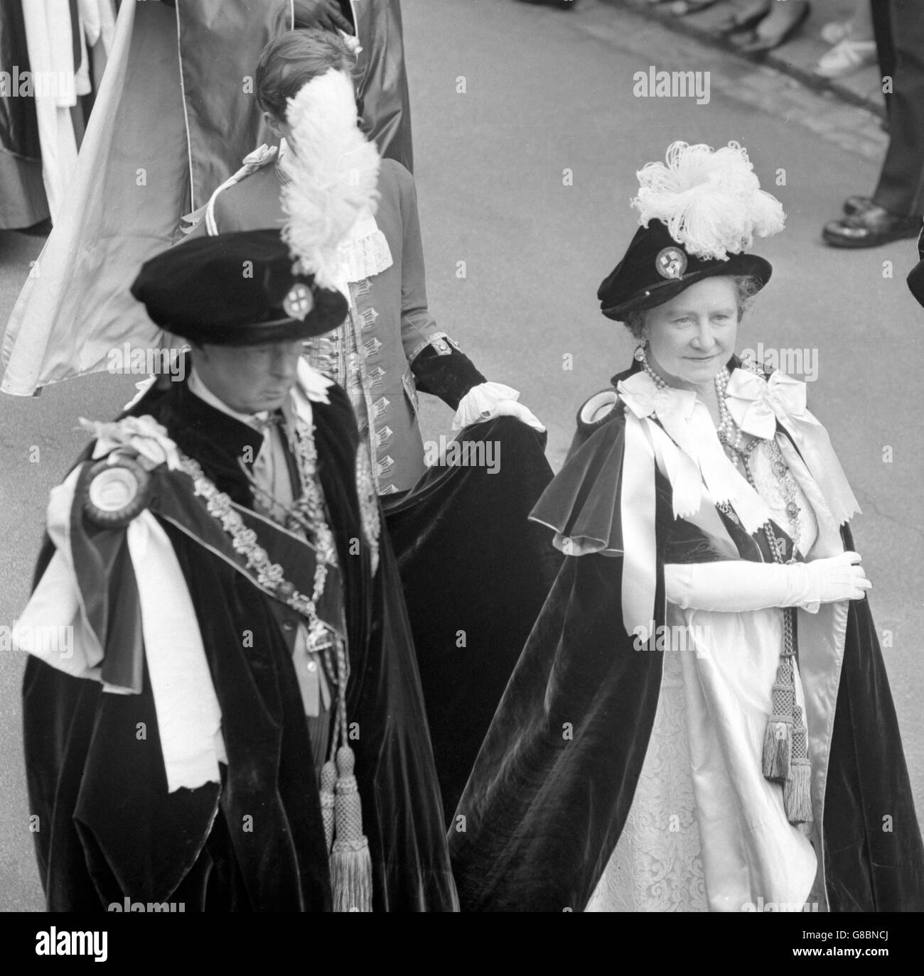 Resplendent in blue velvet mantles and hats ornamented with ostrich plumes, Queen Elizabeth the Queen Mother walks in procession with the Duke of Norfolk at Windsor Castle. They are to attend the Order of the Garter Service in St George's Chapel. Stock Photo