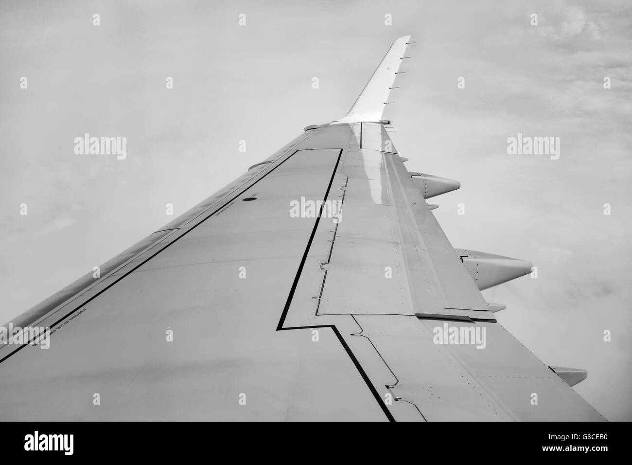 Monochrome image of an aircraft wing above grey clouds Stock Photo