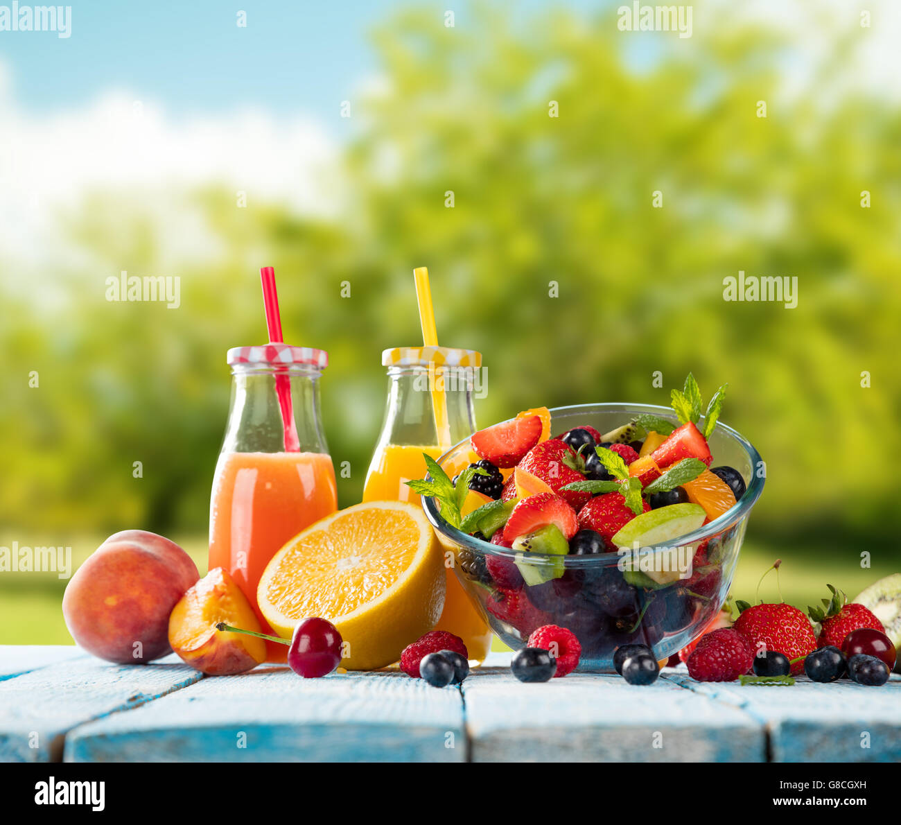 Fresh glasses of juice and salad with fruit mix placed on wooden planks. blur garden on background. Concept of healthy eating, a Stock Photo