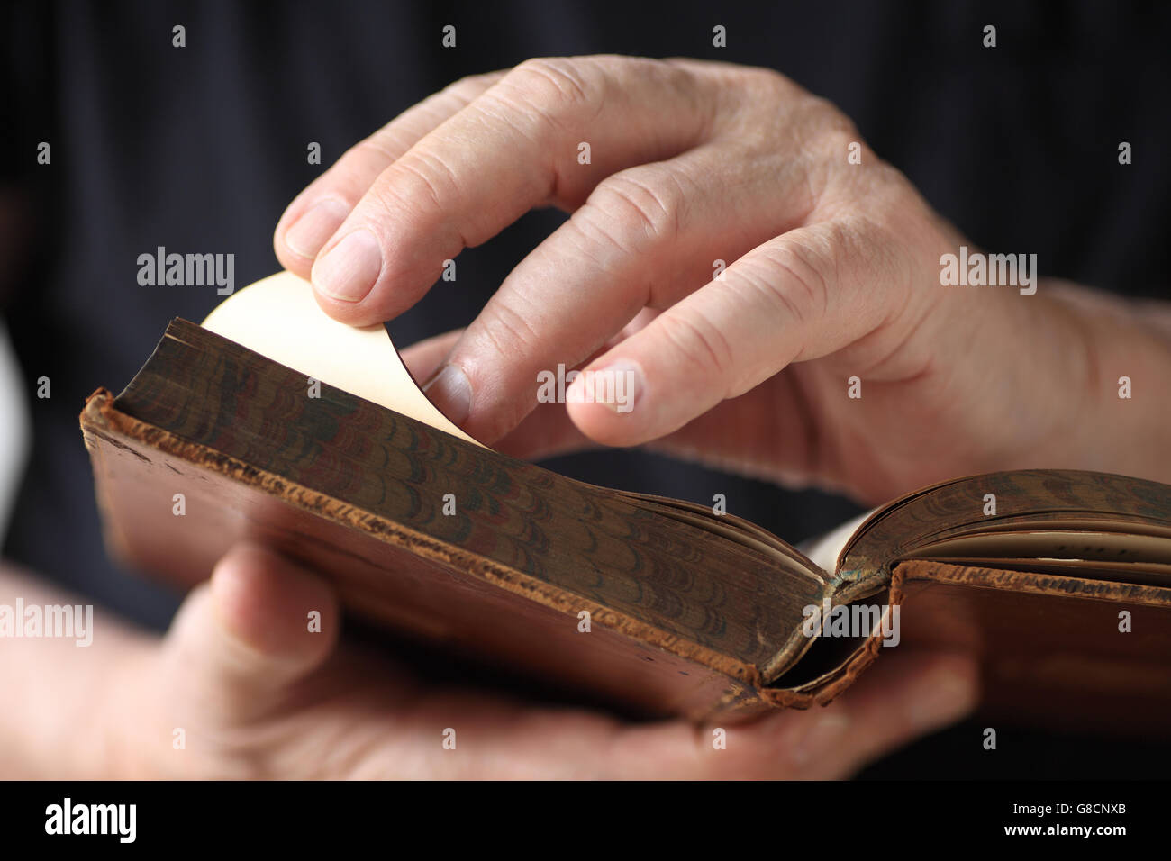 A senior man holds an antique book, and turns a page. Stock Photo