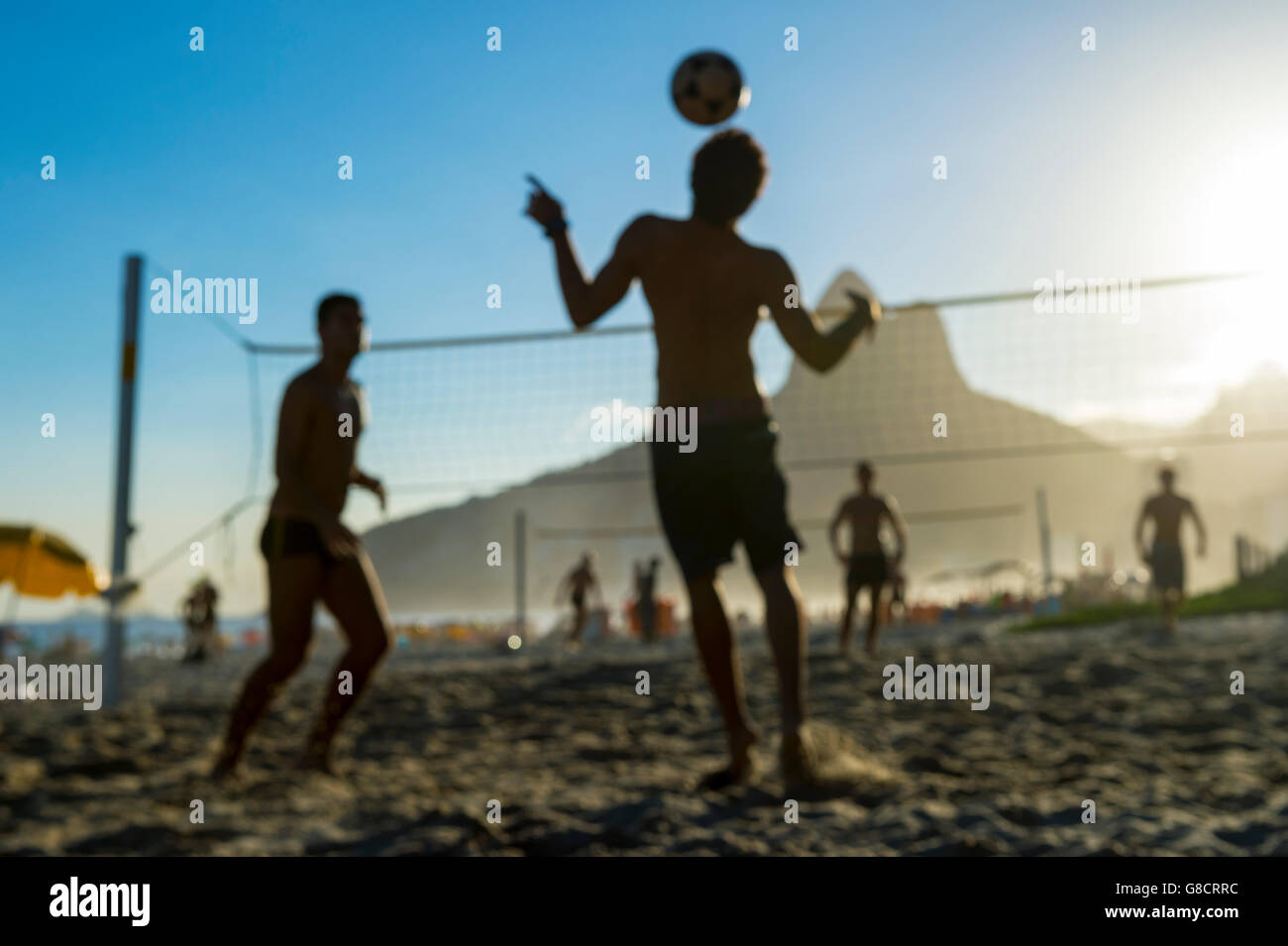 Defocused scene of silhouettes of Brazilians playing futevolei (footvolley) against a sunset backdrop of Ipanema Beach Stock Photo