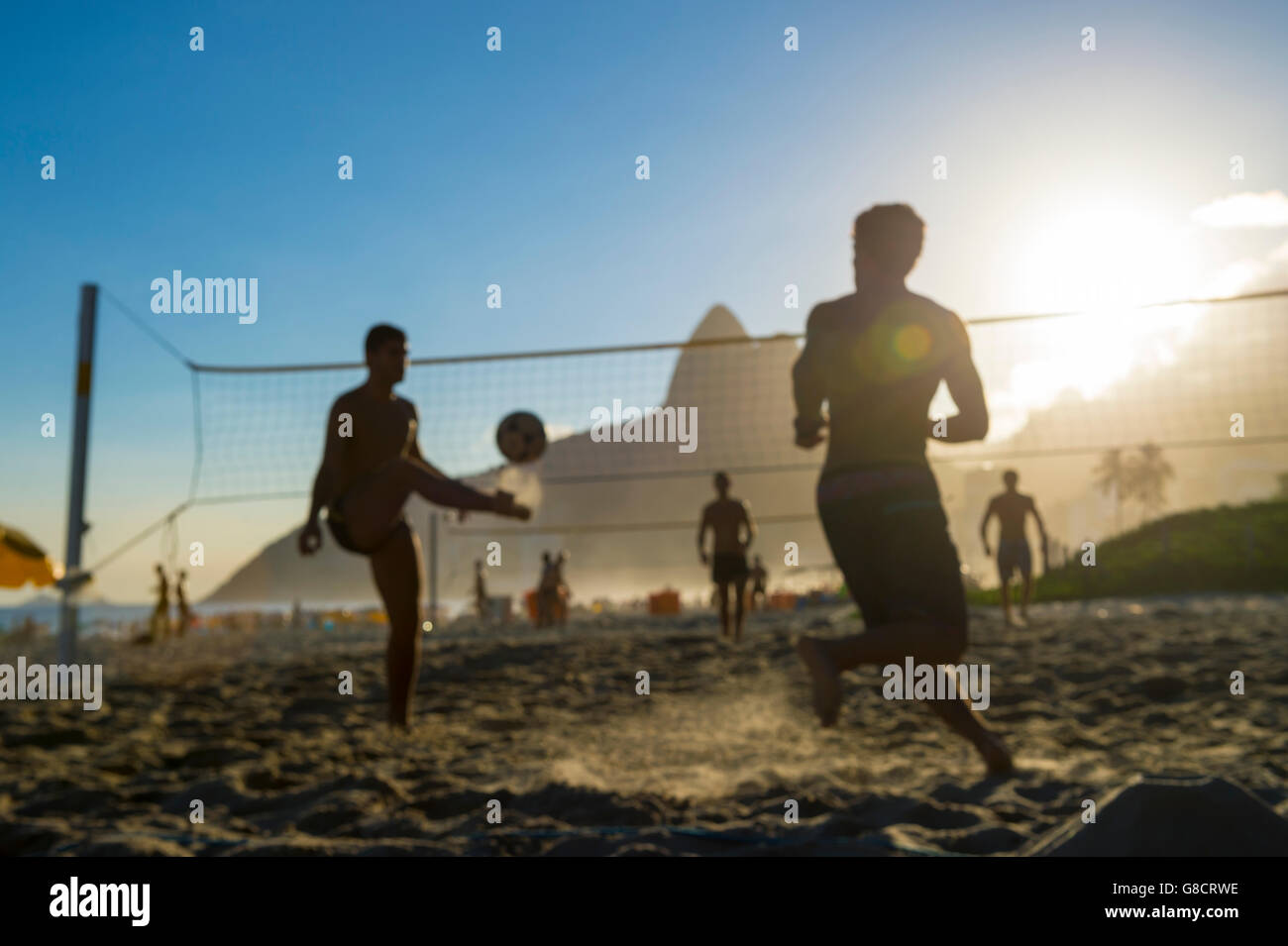 Defocused scene of silhouettes of Brazilians playing futevolei (footvolley) against a sunset backdrop on Ipanema Beach Stock Photo