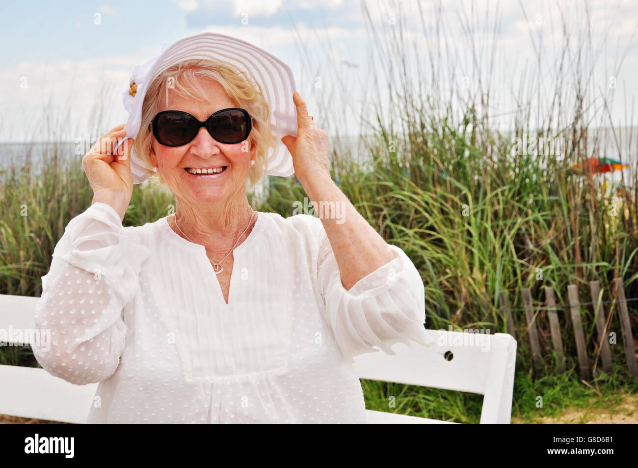 Beautiful and healthy older woman wearing a hat and sunglasses at the beach Stock Photo