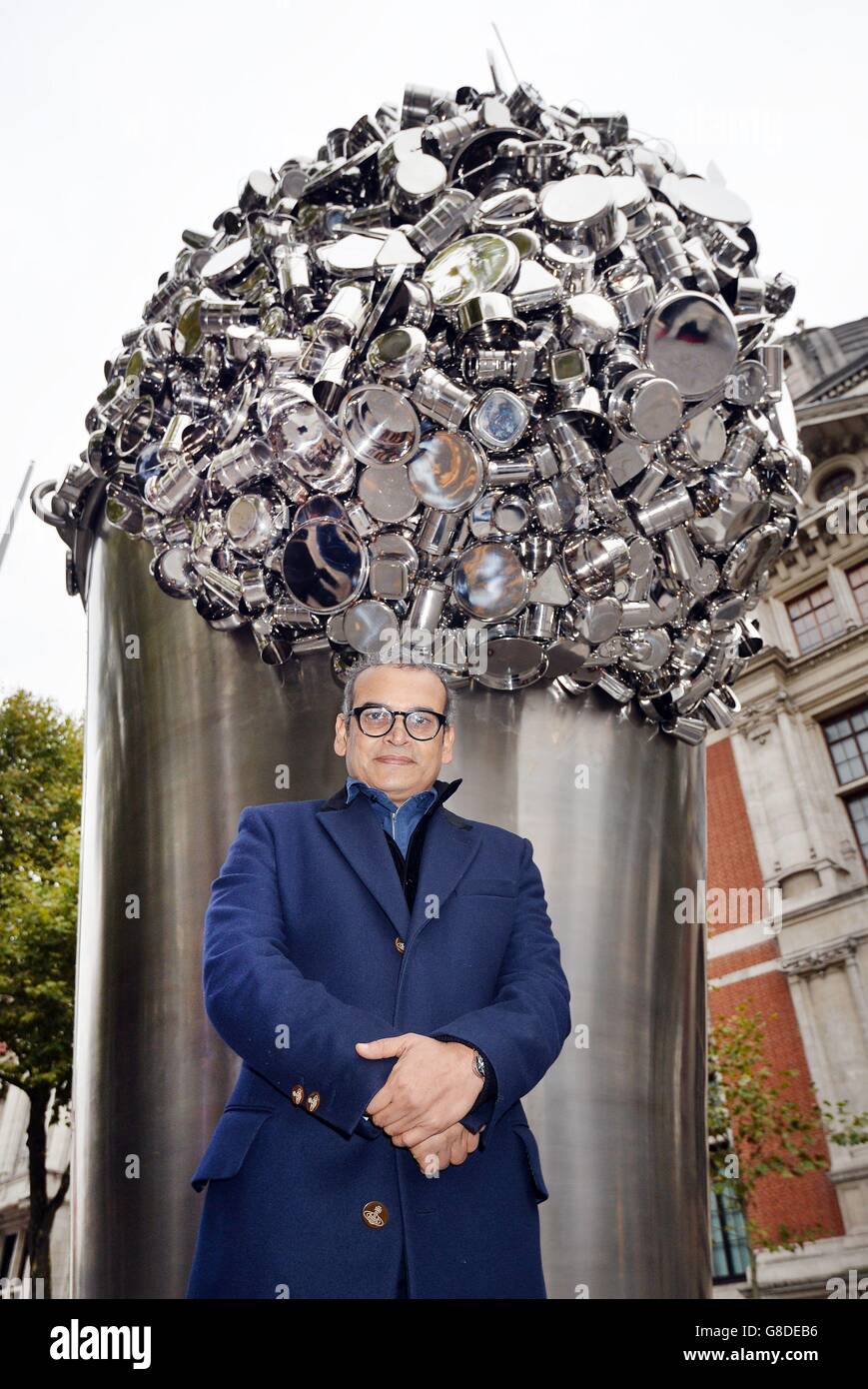 Contemporary Indian artist Subodh Gupta stands in front of his latest installation 'When Soak Becomes Spill', a six metre high stainless steel bucket overflowing with hundreds of pots, pans and cooking containers, which stands outside the Victoria and Albert Museum in Kensington, London. Stock Photo