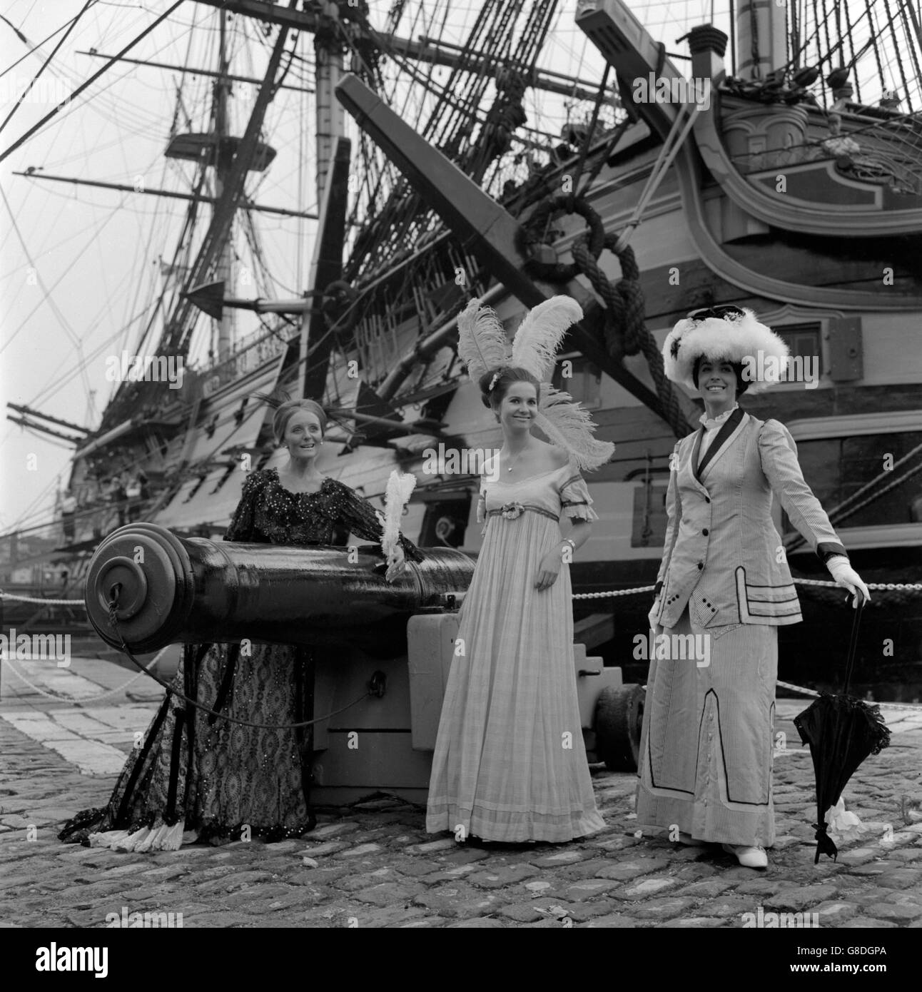 Nelson's flagship Victory makes an effective set-piece for period costumes from the collection of Mrs Paddy Rabbit, of Old Portsmouth. (l-r) Odile Perring, of Antwerp, wears an 1890 dress that once belonged to Queen Alexandria; Jane Price, of Portsmouth, models a Regency-day dress with feathered headdress; and Angela Jarmain, of London, is in a 1900 walking-out dress. The girls model for Mrs Rabbit in charity shows of the period costumes. Stock Photo