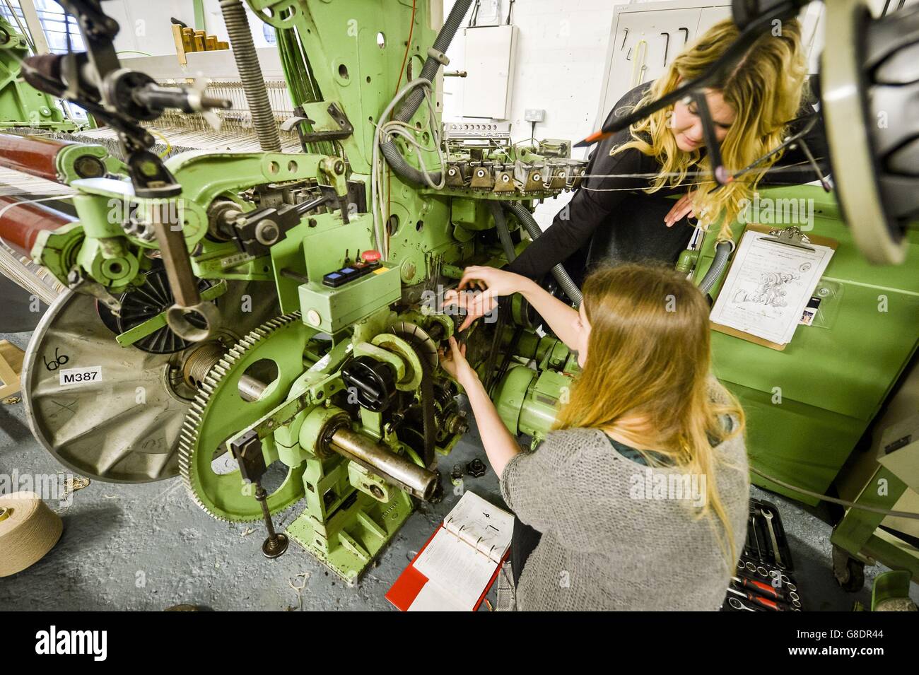 Director of Design and Production Laylah Cook ,24, top, assists Director Juliet Bailey, 33, as she changes a cog on a 1980's loom, made by Dornier, the same company responsible for the World War II German Light Bomber, the Dornier Do 17, at The Bristol Weaving Mill, the first working cloth mill in Bristol in nearly 100 years - which is entirely run by women. Stock Photo