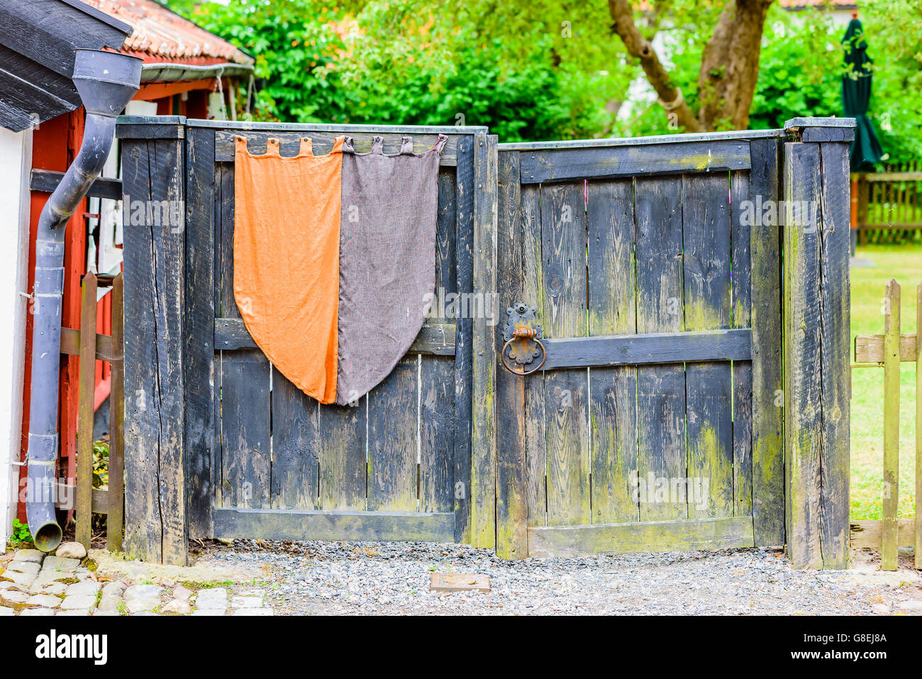 Black old wooden gate with vintage banner. Gate is closed and has a very old locking mechanism and handle. Stock Photo
