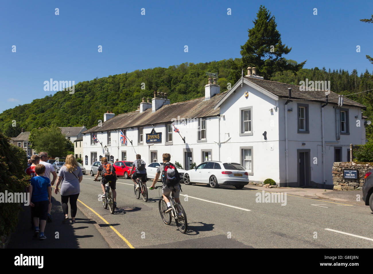 Cyclists and pedestrian visitors passing The Sun inn on the B5320 in Pooley Bridge in the English Lake District. Stock Photo