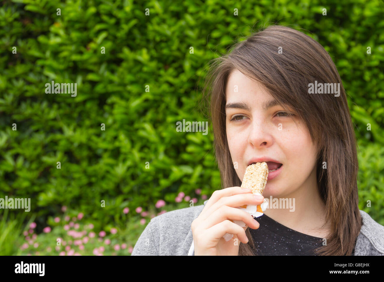Young woman, adult or late teens, headshot in a park eating a cereal bar. Stock Photo