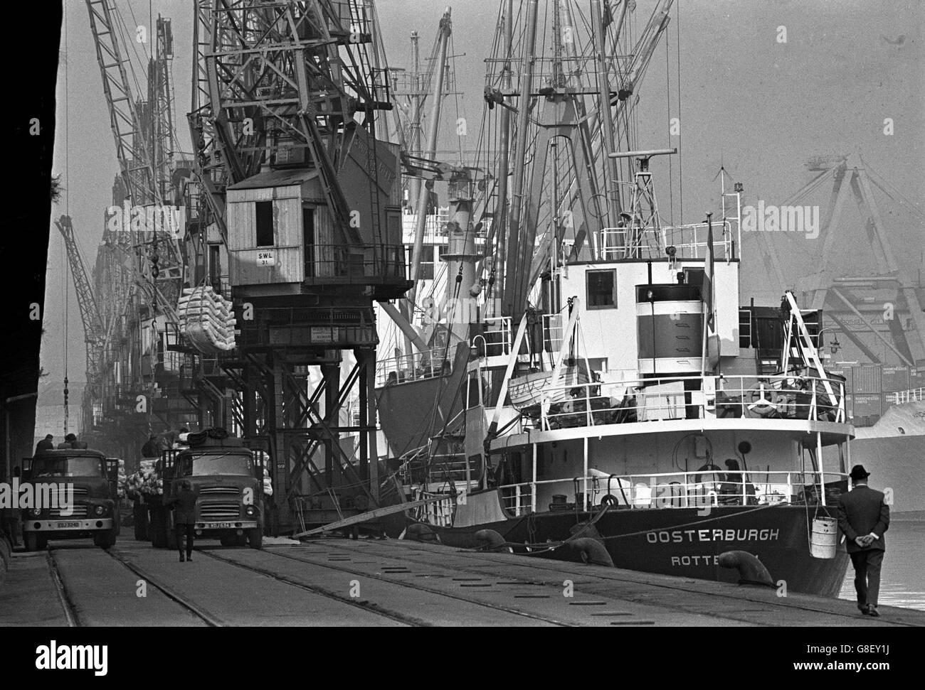 Back at work after the strike, dockers start to tackle the vast backlog of merchandise. Cranes swing into action as lorries waiting on the railway tracks, load up with some of the cargo from the berthed ships. A vessel from Rotterdam is seen in the foreground. Stock Photo