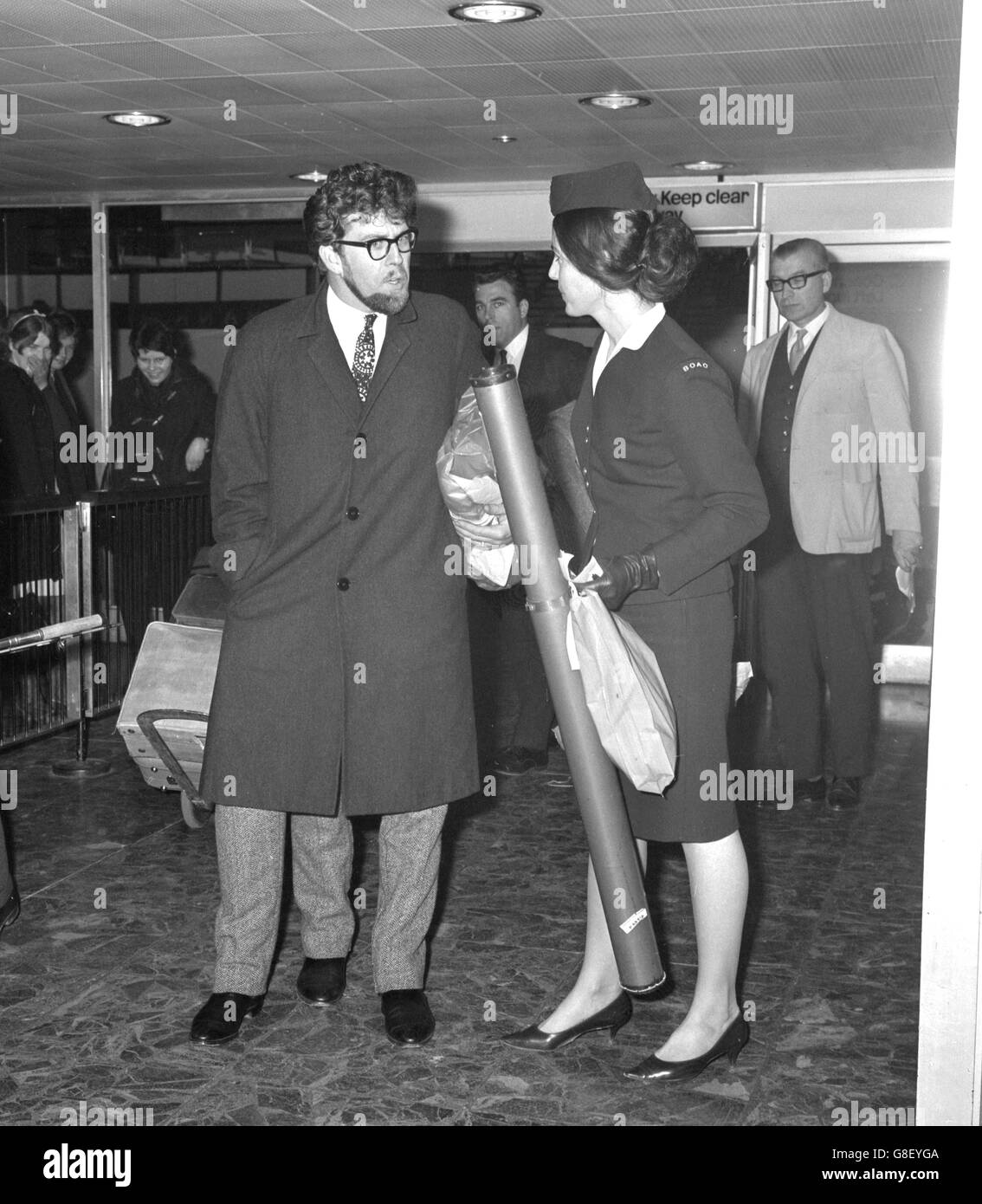 Australian singer Rolf Harris explains the complexity of having three legs to a BOAC official at London Airport, who it seems isn't quite certain whether to be serious or not. Stock Photo