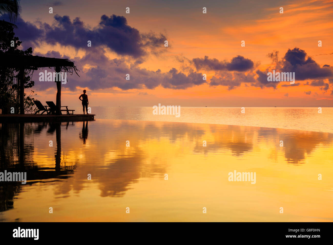 Dawn at an infinity pool - figure silhouetted against an orange sky ...