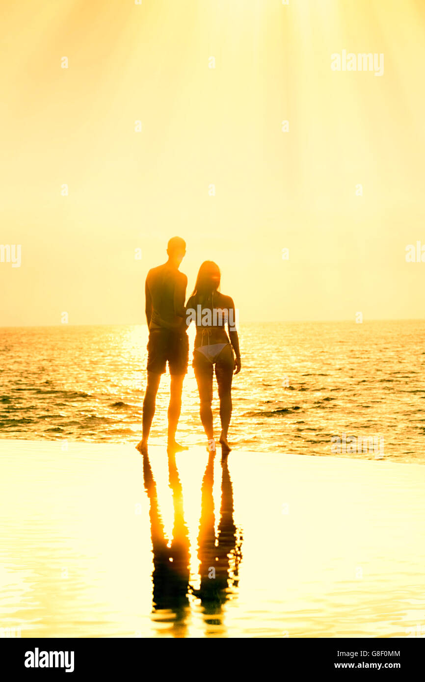 Honeymoon couple standing together at the edge of an infinity pool against a golden sunset/dawn Stock Photo