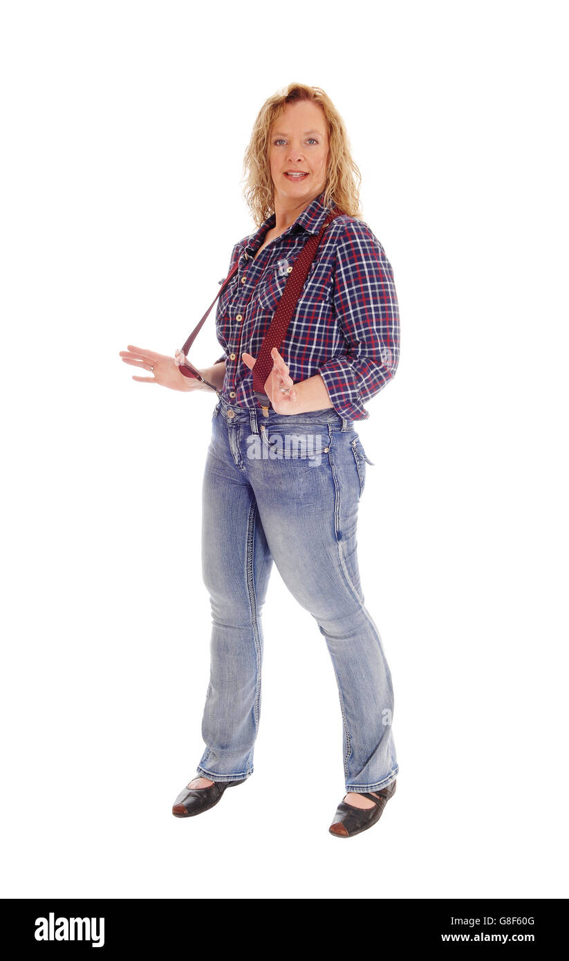 A middle age lovely woman standing isolated for white background in  jeans and checkered shirt holding her red suspender. Stock Photo