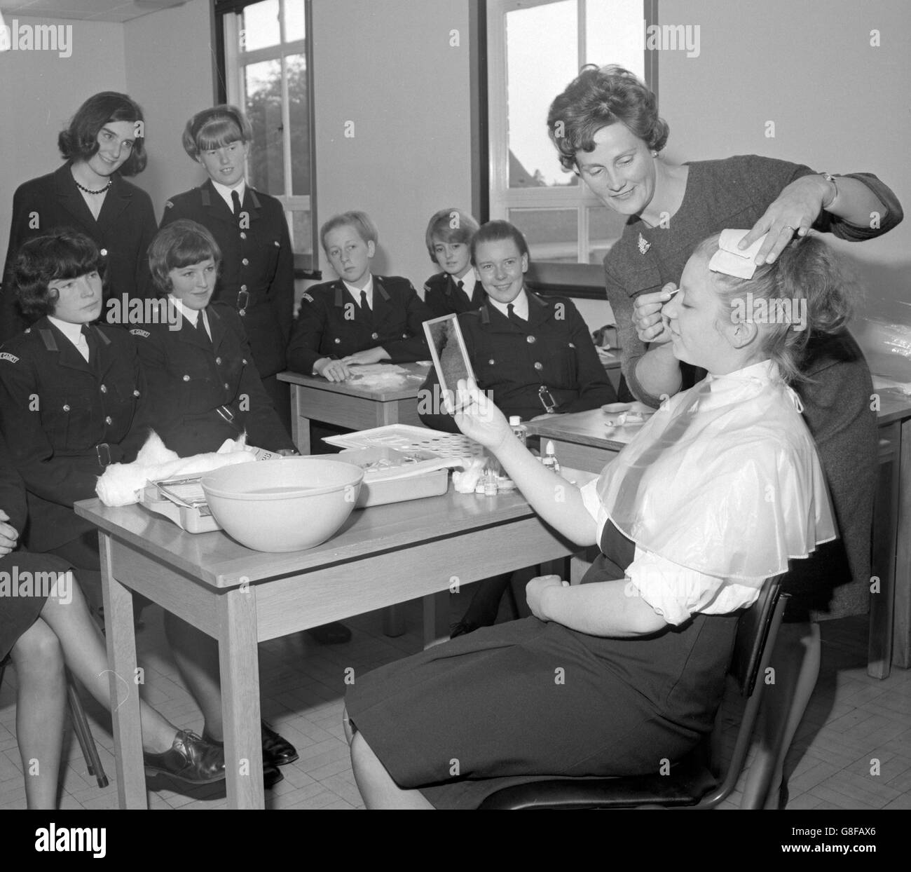Staffordshire County Police girl cadets are given beauty lessons, including instruction on make-up, from professional beautician Eileen Fuggle, of Stafford. She is pictured making-up Sandra Bywater, 18-year-old cadet from Lichfield, Staffordshire, as other members of her class look on. Stock Photo