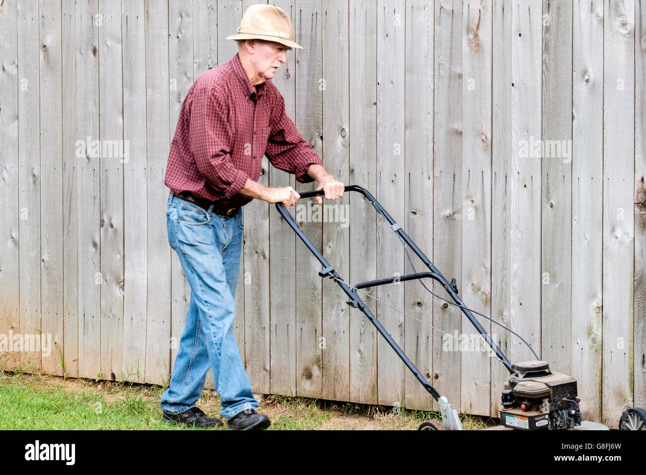 A senior Caucasian man mows his lawn during summer wearing a hat for sun protection. USA. Stock Photo