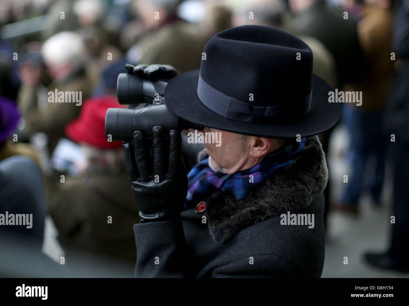 A racegoers watches through binoculars during day one of The International at Cheltenham Racecourse. Stock Photo
