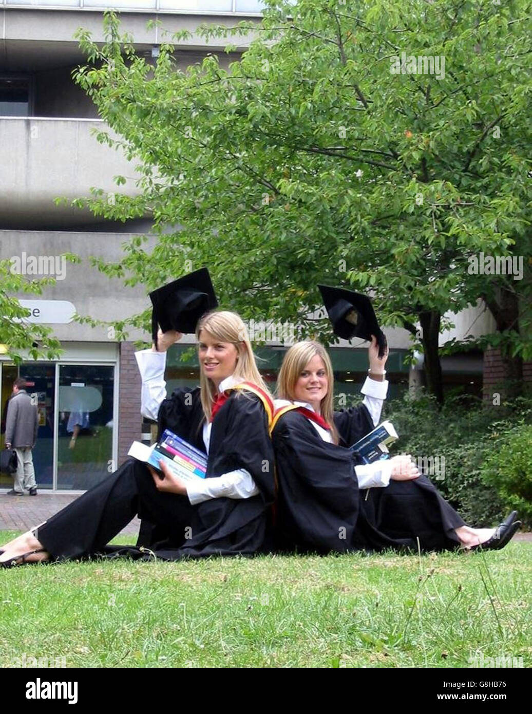 Twins Laura (left) and Helen Taylor in their gowns and mortar boards, after graduating from the same course, with the same class of degree, from the same university. They collected first-class honours degrees in human resource management. Laura and Helen, 22, from Birtley, Tyne & Wear, did the same A-levels at school and, although they were in separate classes, always came out with the same grades. Stock Photo
