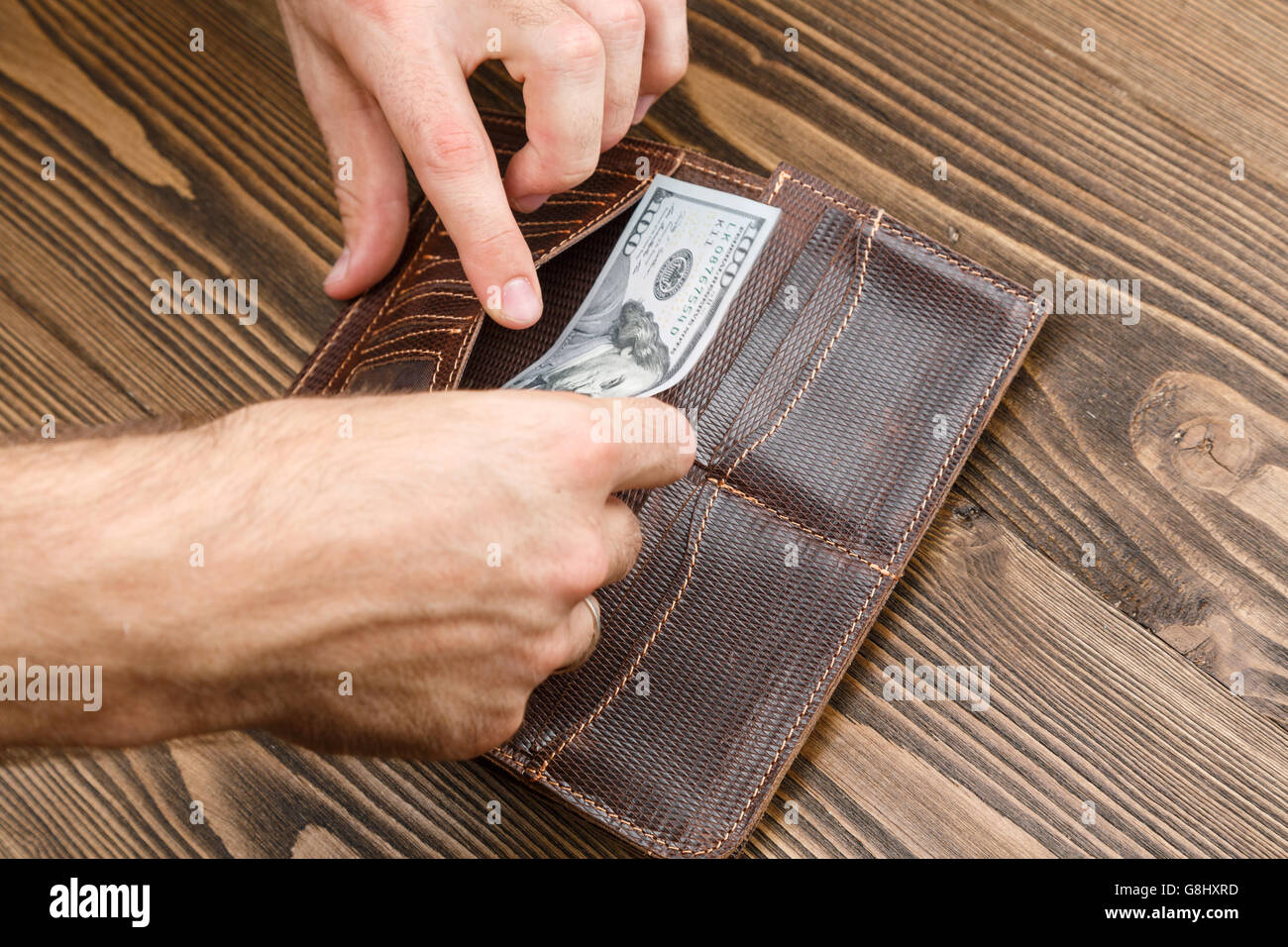 Putting Wallet man is putting 100 dollar banknote in a brown leather wallet over dark ...