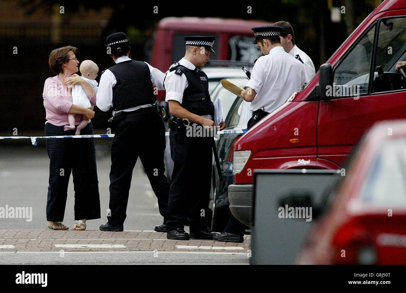 A mother with her baby speaks to police as they raise the cordon, allowing people to return to their homes after sealing off an area of Notting Hill following raids in connection with the attempted bombings last week. Stock Photo