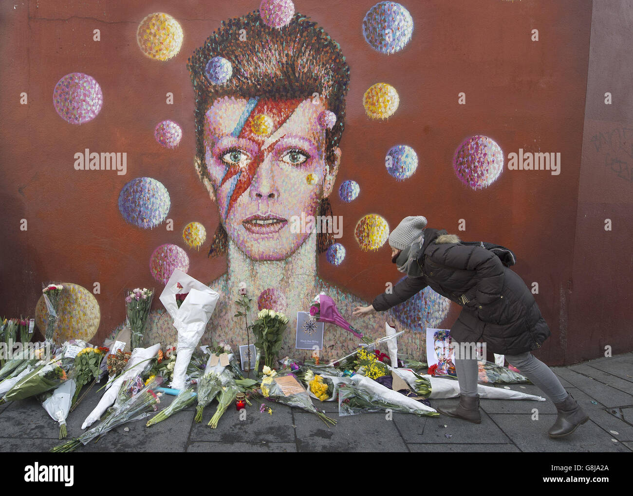Flowers are left below a mural of David Bowie on the wall of a Morley's store in Brixton, London, the singers birthplace, after the rock star died following an 18-month battle with cancer. Stock Photo