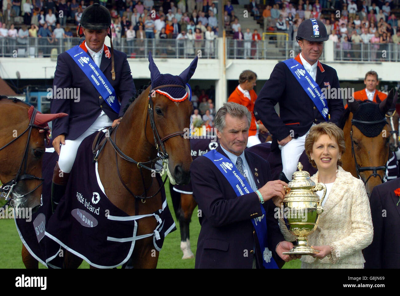 Great Britain's Chef d'Equipe, Derek Ricketts accepts the Aga Khan Challenge Trophy from President Mary McAleese as riders William Funnel on Cortaflex Mondriaan (left) and Michael Whitaker on Portofino 63 (right) look on at the Failte Ireland Dublin Horse Show, Friday August 5 2005, at the Royal Dublin Society Arena, Dublin. Stock Photo